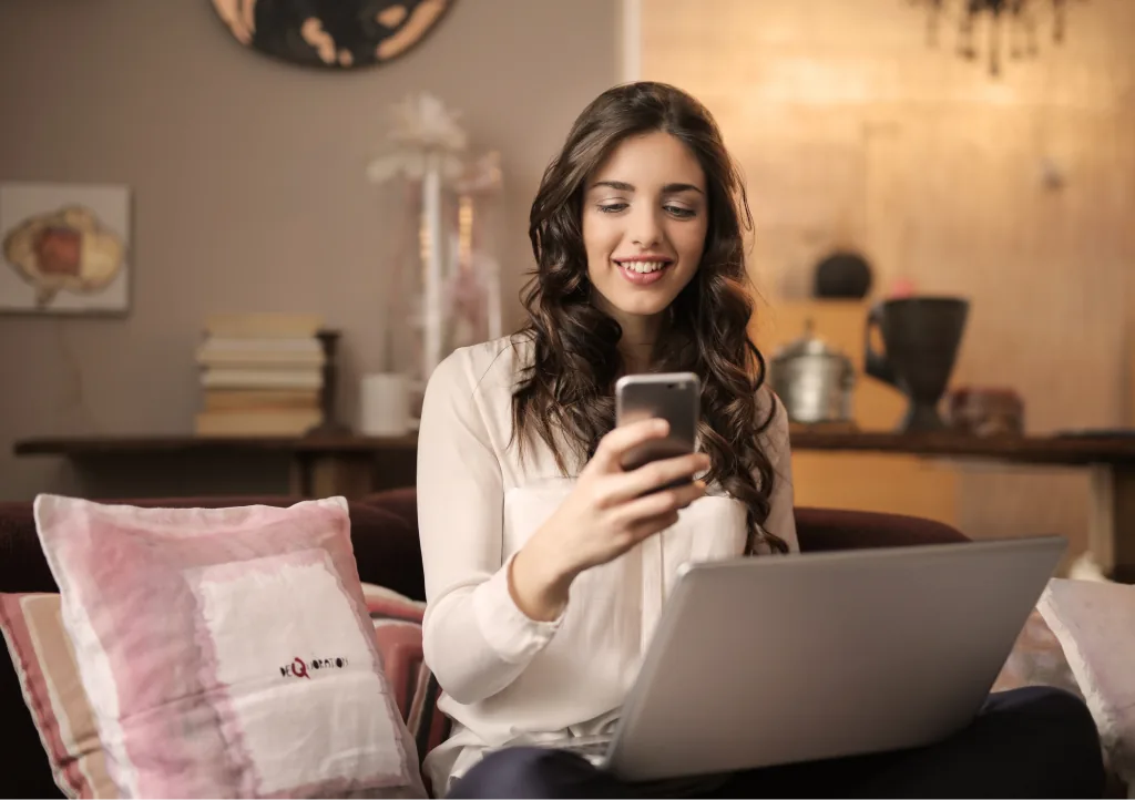 Donna naviga in internet con smartphone e portatile sul divano